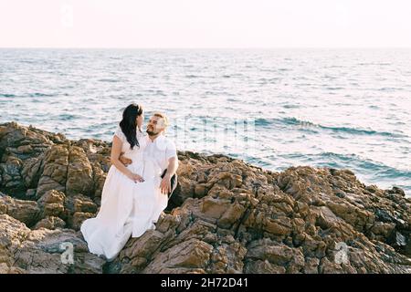Bride sits on the knees of groom on the rocky seashore Stock Photo