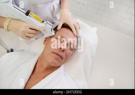Therapist doing facial mesotherapy treatment on middle aged handsome Caucasian man in a modern wellness spa center. Attractive man getting injections Stock Photo