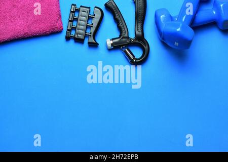 Top view of fitness tools. The dumbbells, hand grips, and towel isolated on a blue background Stock Photo