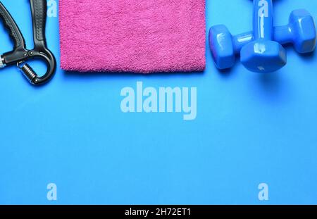 Top view of fitness tools. The dumbbells, hand grips, and towel isolated on a blue background Stock Photo