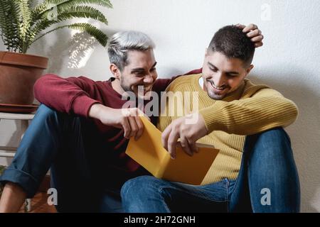 Lgbt gay couple hugging and reading book together indoor at home - Homosexual love and romance concept Stock Photo