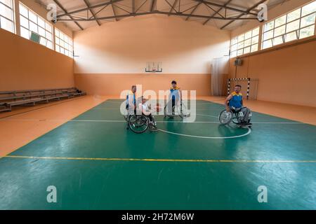 Disabled War veterans mixed race and age basketball teams in wheelchairs playing a training match in a sports gym hall. Handicapped people Stock Photo