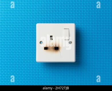 Damaged electrical domestic power socket with cracks and burn marks on a blue background Stock Photo