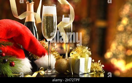 Christmas holidays celebration concept with bottle of sparkling white wine and glasses and christmas hat with gift and shiny ribbon decoration in livi Stock Photo