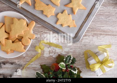 Wooden table with cookies with freshly baked Christmas shapes on a baking tray and plate with Christmas decoration. Top view. Horizontal composition. Stock Photo