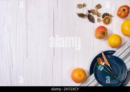 Autumn leaves, blue plates and iridescent silverware on a light wooden table Stock Photo