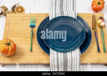 Dinner set with blue plates, iridescent cutlery and pink tomatoes on bamboo table Stock Photo