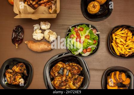 Top view image of Sunday dishes, roast chicken with sauce, lettuce and tomato salad, homemade chips and roasted apples Stock Photo