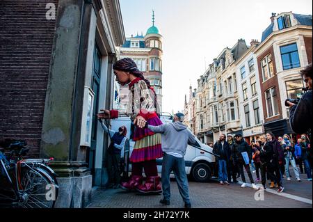 The Hague, Netherlands. 19th Nov, 2021. Little Amal seen knocking on a door on the street.On the last day of her visit to The Netherlands, the the giant puppet 'Little Amal', a nine-year-old Syrian refugee girl and over 11-feet-tall walked around the city center of The Hague, where the House of Representatives is located, to interact with the people on the streets. This visit was organized by Amare, a new cultural hub as a part of the Open Festival. With her visit, Amal wants to grab attention across Europe to the plight of young refugees who have fled from Syria. During her visit to the city  Stock Photo