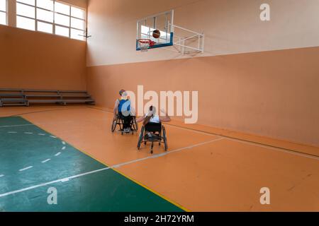 Disabled War veterans mixed race opposing basketball teams in wheelchairs photographed in action while playing an important match in a modern hall.  Stock Photo