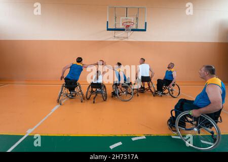 Disabled War veterans mixed race and age basketball teams in wheelchairs playing a training match in a sports gym hall. Handicapped people Stock Photo