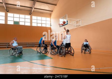 Disabled War veterans mixed race and age basketball teams in wheelchairs playing a training match in a sports gym hall. Handicapped people Stock Photo