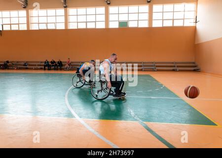 Disabled War veterans mixed race and age basketball teams in wheelchairs playing a training match in a sports gym hall. Handicapped people Stock Photo