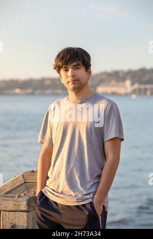 Handsome biracial Asian, Caucasian mixed race young man standing outdoors by lake near sunset Stock Photo