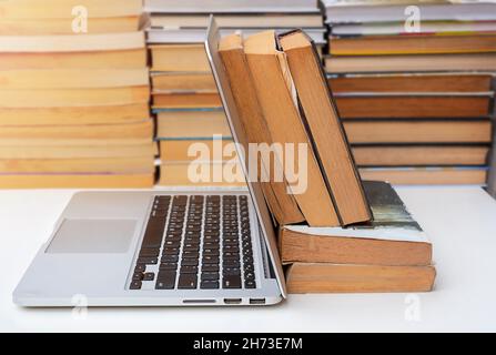 stack of books and a computer on the table against the background of books. e-learning Stock Photo