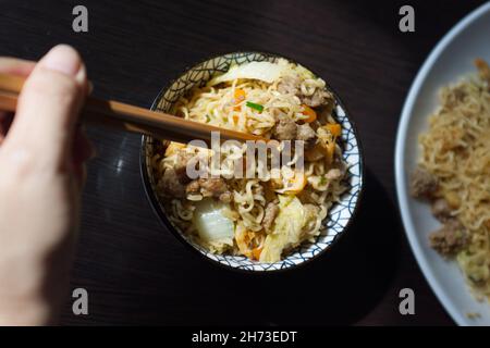 Woman's hand holding chopsticks of instant noodles. Stock Photo