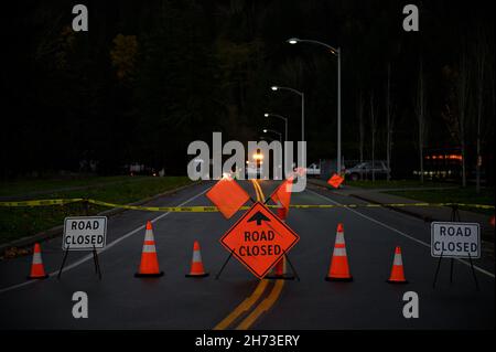 Night photo of a reflective and bright orange construction sign on the street that warns the traffic about a closed road ahead. There is a pilot car a Stock Photo
