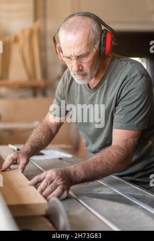 Man with safety glasses cutting wood on sliding table saw Stock Photo