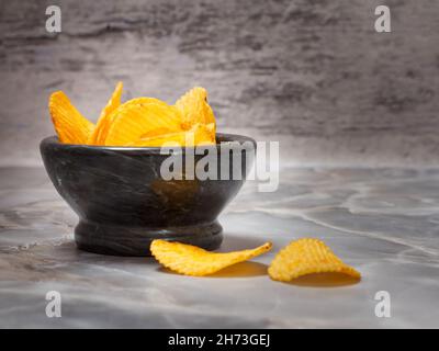 Potato chips in a black stone bowl on the gray background. Stock Photo