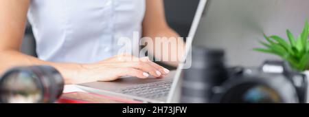 Woman typing on laptop keyboard at table with camera lenses closeup Stock Photo