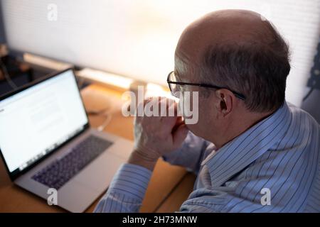Senior man working with laptop computer at home and thinking on document. Stock Photo