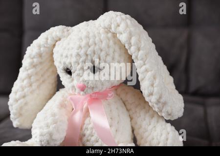 white knitted rabbit with long lashes and pink ribbon on a neck. baby first friend. hand made kids toys. knitting as a hobby Stock Photo