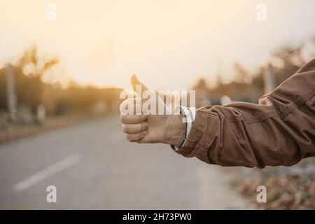 Female hand and hitchhiking sign on road, traveling by autostop in the city. Woman try stop car thumb up. Adventure and tourism concept.