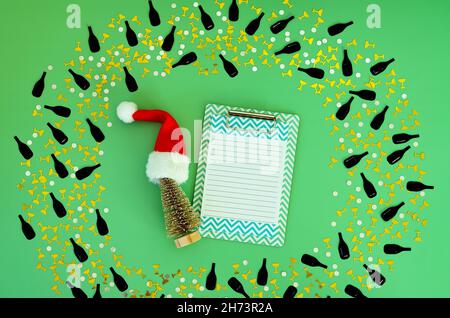Christmas flat lay on green background with place for text. Christmas hat and toy tree, confetti and a notebook. Resolutions, plan, goals, action Stock Photo