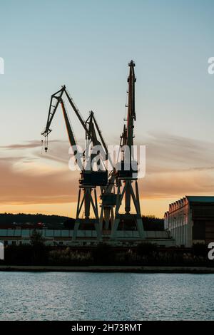 Vertical view of port shipyard cranes against sunset sky Stock Photo