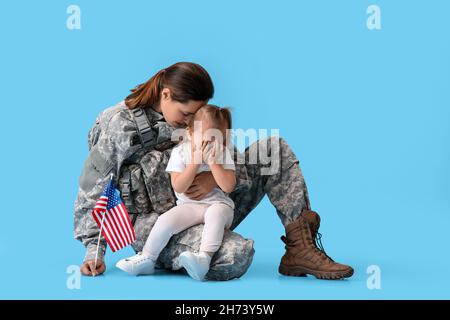 Female soldier and her sad little daughter with USA flag on color background Stock Photo