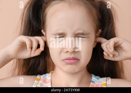 Portrait of little girl closing ears on beige background, closeup Stock Photo