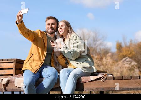 Lovely couple with cute dog taking selfie on autumn day Stock Photo