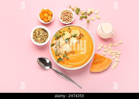 Composition with delicious pumpkin cream soup in bowl and seeds on pink background Stock Photo
