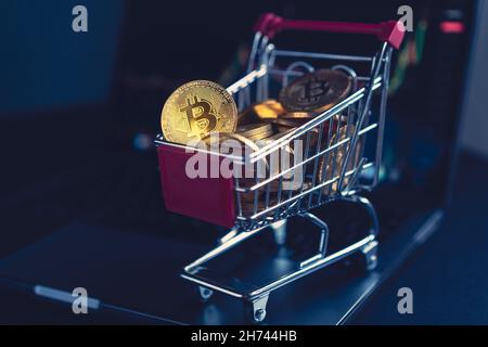 side view closeup cryptocurrency concept of market shopping cart full of bitcoin golden crypto coins standing near a notebook computer screen with tra Stock Photo