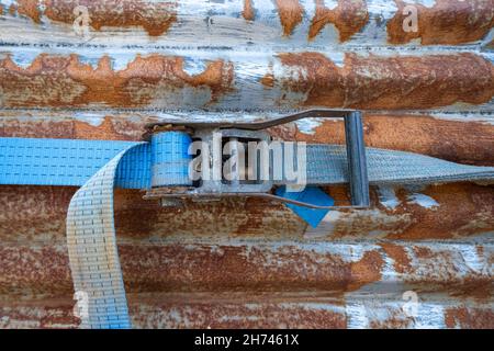 A blue rachet strap wrapped around a rusty corrugated iron metal sheet Stock Photo