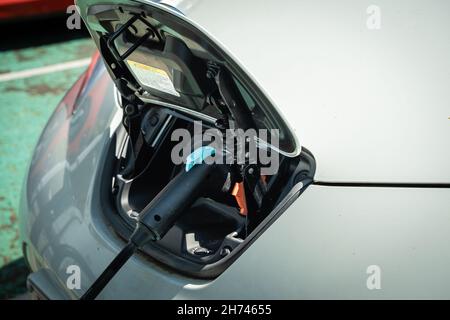 Electric vehicle with a front charging port plugged in and charging the car battery Stock Photo