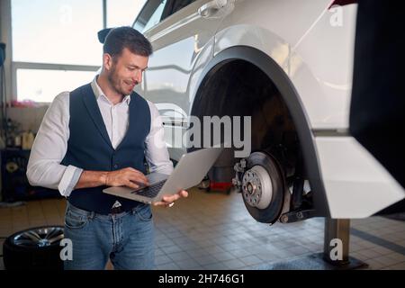 Mechanic Using Laptop While Examining Car Engine. Fixing Stock Photo