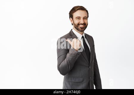 Handsome corporate man in business clothes pointing left, inviting clients, showing company sign and smiling, standing over white background Stock Photo