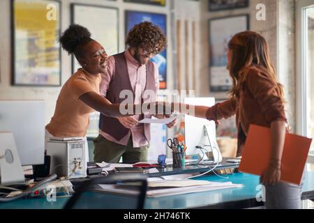 afro american and caucasian females shaking hands over the desk in office with beardy male holding and reading document Stock Photo