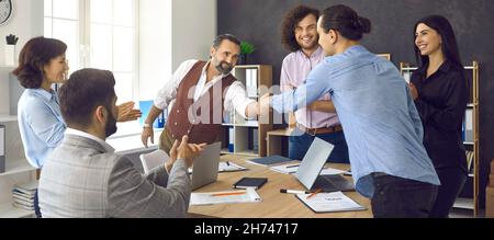 Two happy people making a deal and shaking hands in a business meeting with colleagues Stock Photo