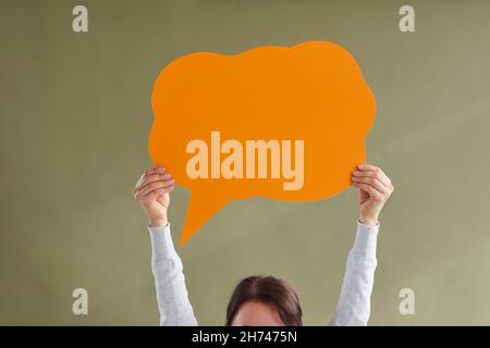 Woman holding one orange blank free speech bubble layout with place for text on green background. Stock Photo