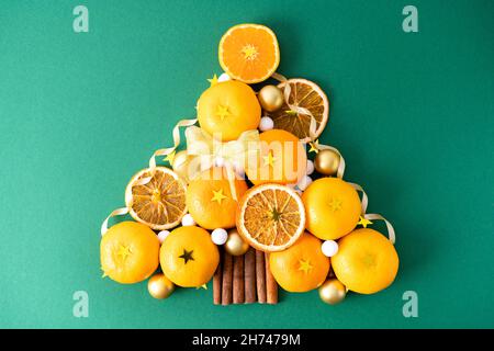 Christmas tree made from fresh tangerines with Christmas decorations with cinnamon on a green background. Creative concept for a Christmas card. Stock Photo