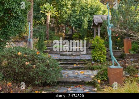 A set of rustic stone steps leading up through the garden past the shrubs, chinese windmill ferns and woodland to the magical doorway at the top Stock Photo