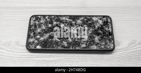 Modern touch screen smartphone with broken screen full of cracks on wooden background. Repair gadget concept Stock Photo
