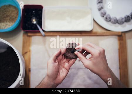 Hands holding cocoa dough and raisin on background work table with other ingredients. Preparation of Christmas sweets during advent. Stock Photo
