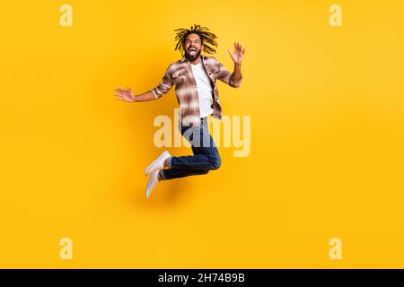 Full length body size photo of man jumping high wearing casual clothes laughing isolated on vivid yellow color background