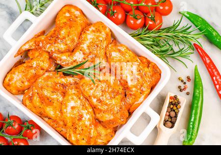 Marinated chicken wings in red sauce in a white ceramic plate for oven baking with vegetables. Oven baking wings. Semifinished. Fast cooking.Raw Stock Photo