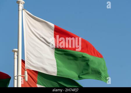 Madagascar Flag hanging and blowing in sunshine on blue sky background. Stock Photo