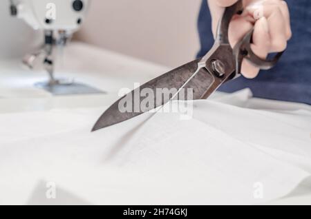 Vintage tailor's scissors cut white fabric. Stock Photo