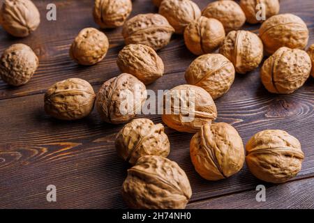 many walnuts with shells randomly scattered on brown wooden surface Stock Photo